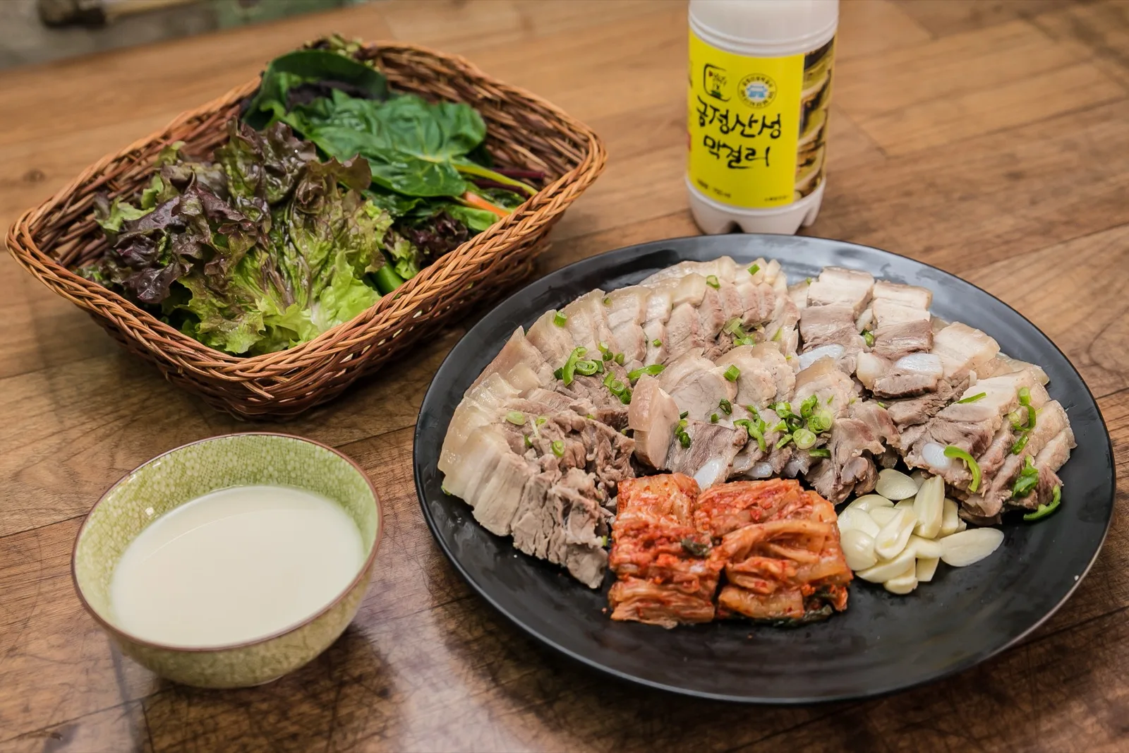 수육 한 접시와 김치, 마늘, 쌈채소, 막걸리 상차림
